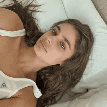 a woman in a white tank top is laying on a bed with her eyes closed