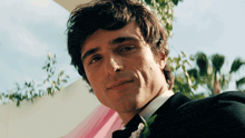 a man in a tuxedo with a flower in his lapel looks at the camera
