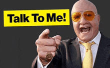 a bald man in a suit and tie is pointing at the camera with the words talk to me behind him