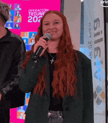 a woman with red hair is holding a microphone in front of a pink sign that says operacion triunf 202