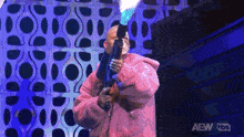 a man in a pink coat is holding a flamethrower on stage .