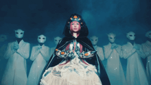 a woman in a cape stands in front of a group of people wearing white masks
