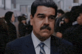 a man with a mustache wearing a suit and tie stands in a crowd