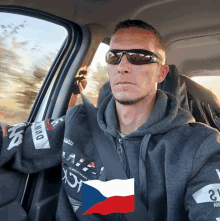 a man wearing sunglasses is sitting in a car with a czech flag in the background