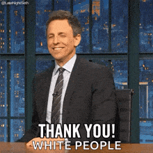 a man in a suit and tie is sitting at a desk and saying thank you white people