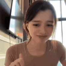 a young woman is giving a thumbs up sign while sitting at a table in front of a television .