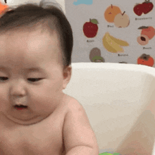 a baby is taking a bath in a bathtub with a picture of fruit on the wall behind him .