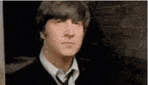 john lennon is wearing a suit and tie and looking at the camera .