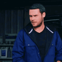 a man wearing a blue jacket and black shirt stands in front of a shelf with bottles of chemicals on it