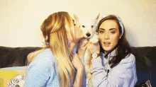 two women are sitting on a couch kissing a dog