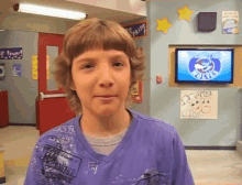 a boy in a purple shirt stands in front of a wall with a sign that says ' pride ' on it