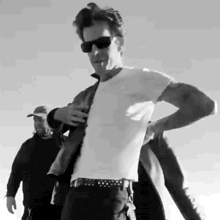 a man wearing sunglasses and a white shirt is standing in front of a group of people .