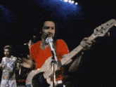 a man in a blue shirt is playing a guitar and singing into a microphone on stage .
