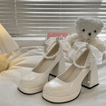 a pair of white shoes with pearls and a teddy bear on a bed .