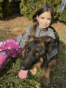 a little girl laying on the grass with a german shepherd dog