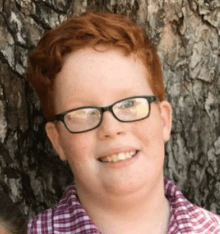 a young boy with red hair wearing glasses and a plaid shirt