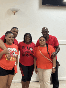 a group of people are posing for a picture and one of them is wearing a black popular demand shirt