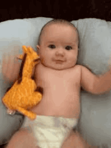 a baby in a diaper is laying on a pillow holding a stuffed giraffe toy .