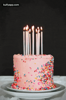 a pink birthday cake with candles and sprinkles on a plate