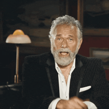 a man with gray hair and a beard points at the camera