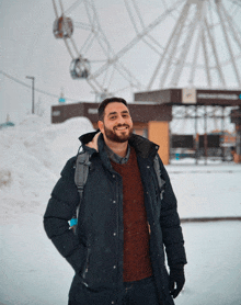 a man stands in front of a large ferris wheel in the snow