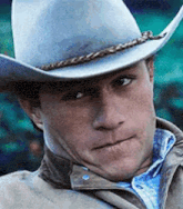 a man wearing a cowboy hat and a jacket is looking at the camera .