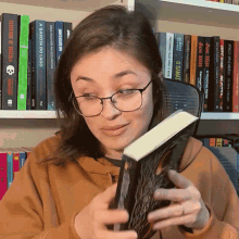 a woman wearing glasses holds a book in front of a bookshelf with a book titled a garota do lago