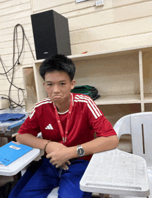 a young boy wearing a red adidas shirt sits at a desk