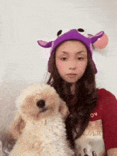 a girl wearing a purple hat holds a dog