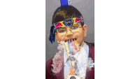 a young boy wearing glasses and a red bull headband is smoking a cigarette while wearing a medal .