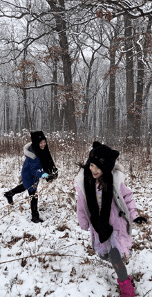 two little girls are playing in the snow and one has a cat hat on