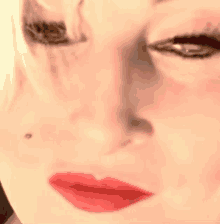 a close up of a woman 's face with red lips and a black spot on her nose .