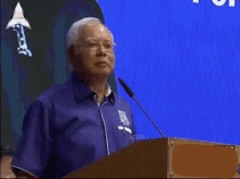 a man is standing at a podium giving a speech and the words bodo punya kerja are on the screen behind him .