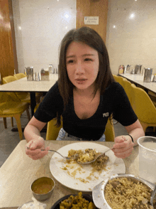 a woman is sitting at a table with a plate of food and a spoon in her hand with a shirt that says yeu