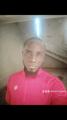 a man in a red shirt is taking a selfie in front of stairs .