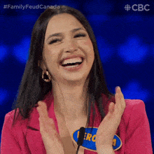 a woman in a pink jacket is laughing and clapping her hands while sitting in front of a microphone .