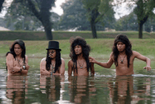 a group of men are standing in a body of water with one wearing a top hat