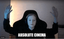 a young boy sitting in a chair with his hands in the air and the words absolute cinema on the screen