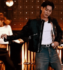 a man wearing a black leather jacket and a white shirt is dancing in a bar .