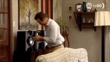 a man is playing a record player in a living room with a tvgo logo in the corner