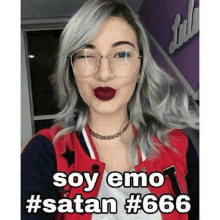 a woman wearing glasses and a red jacket is taking a selfie and says `` soy emo # satan # 666 '' .