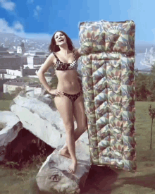 a woman in a bikini is standing on a rock next to a large mattress