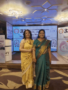 two women pose for a photo in front of a sign that says annual upcog conference