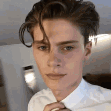 a young man in a white shirt and tie is taking a selfie .