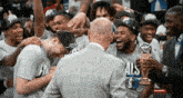 a man in a suit holds a trophy in front of a group of basketball players wearing shirts that say als