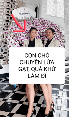 two women standing in front of a sign that says " con cho chuyen lua gat qua khu lam di "