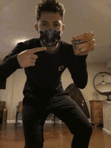 a man wearing a mask holds a package of top ramen noodles