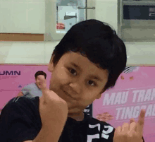 a young boy giving the middle finger in front of a sign that says mau tran