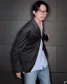 a man wearing glasses and a jacket is standing in front of a wall