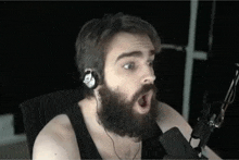 a man with a beard wearing headphones and a microphone is making a surprised face .